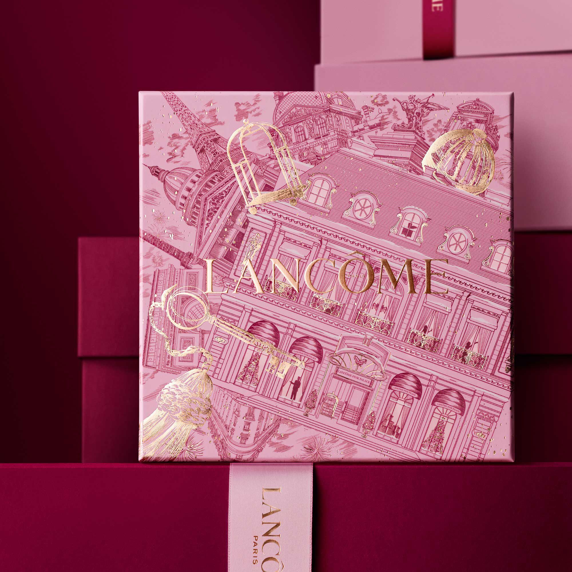 Image of pink Lancome holiday gift box standing in front of a pile of pink and dark red gift boxes, set against a dark red background.