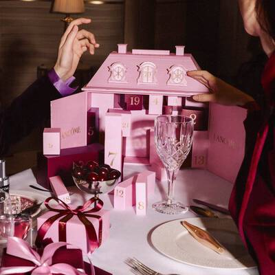 Hands interacting with a pink Lancome advent calendar on a festive dining table with tableware and cherries.