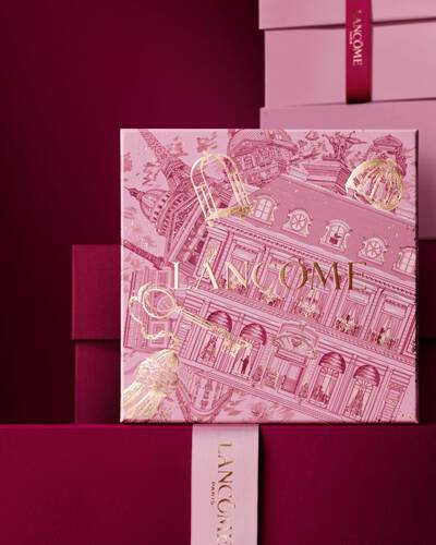 An elegant stack of pink and deep burgundy Lancome gift boxes, featuring a central box detailed with gold Parisian architectural illustrations.