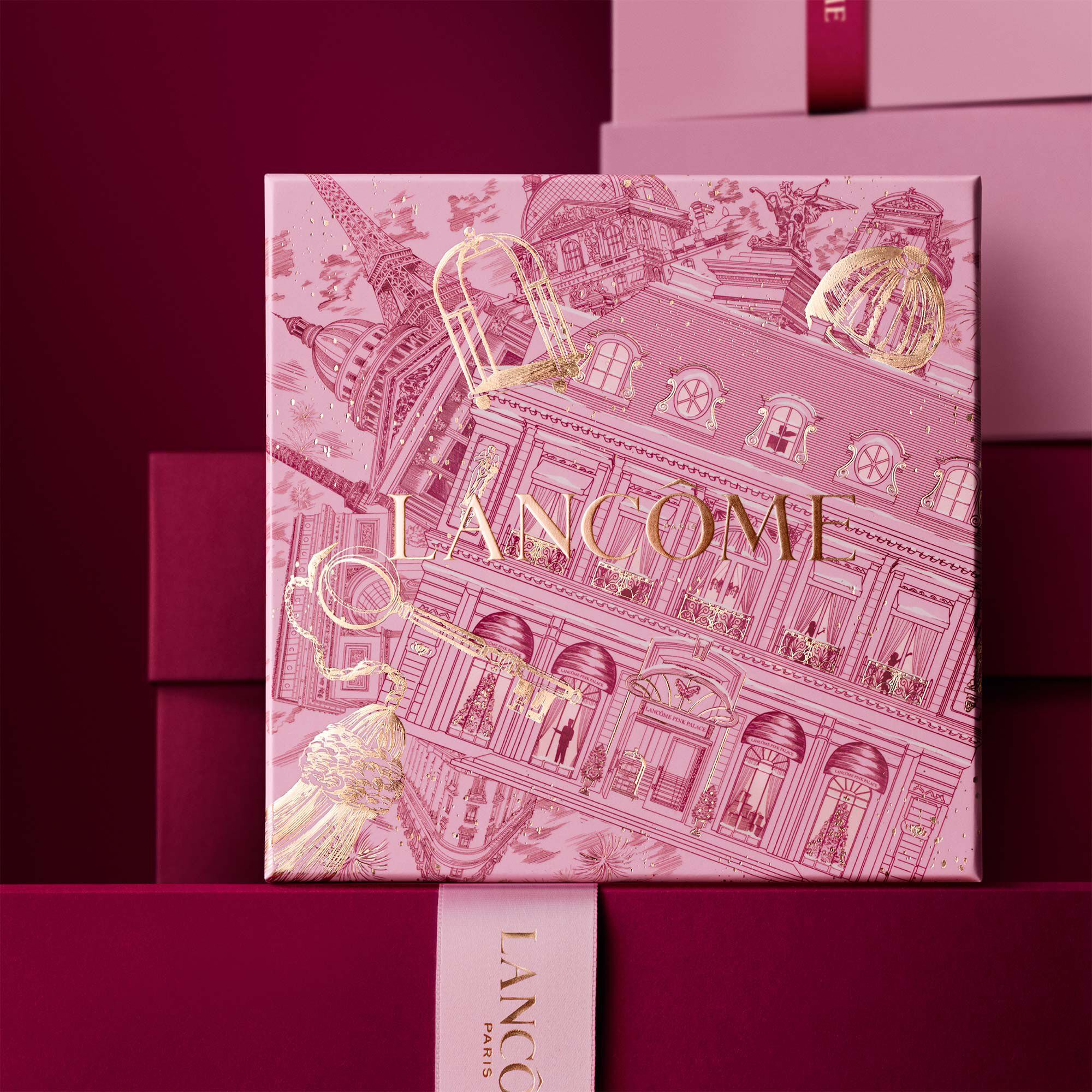 Image of pink Lancome holiday gift box standing in front of a pile of pink and dark red gift boxes, set against a dark red background.