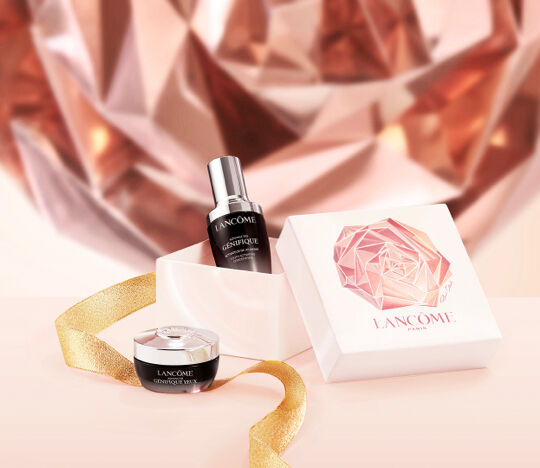 A luxurious skincare display featuring Lancome's Genifique serum and cream, elegantly presented in a white box with a gold ribbon, set against a soft-focus background resembling a rose.