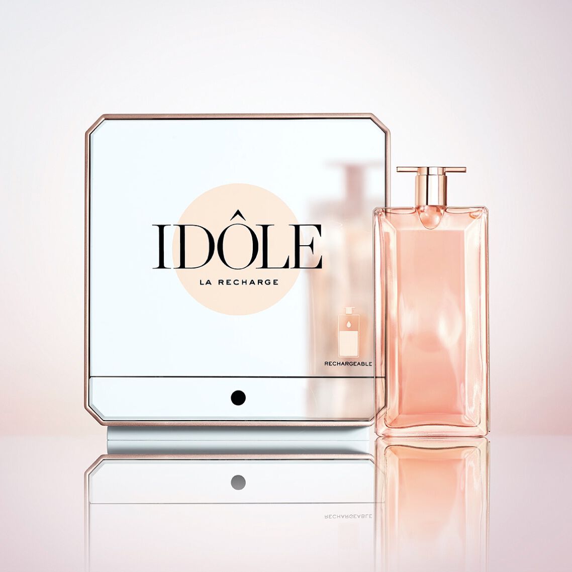 A sleek, modern perfume bottle with a soft pink liquid is displayed next to a reflective square container labeled "IDOLE LA RECHARGE." The design features a minimalist aesthetic with elegant lines.