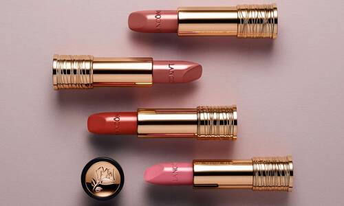 A collection of four luxurious lipsticks with gold tubes, featuring shades of pink and coral, arranged neatly on a soft, neutral background.