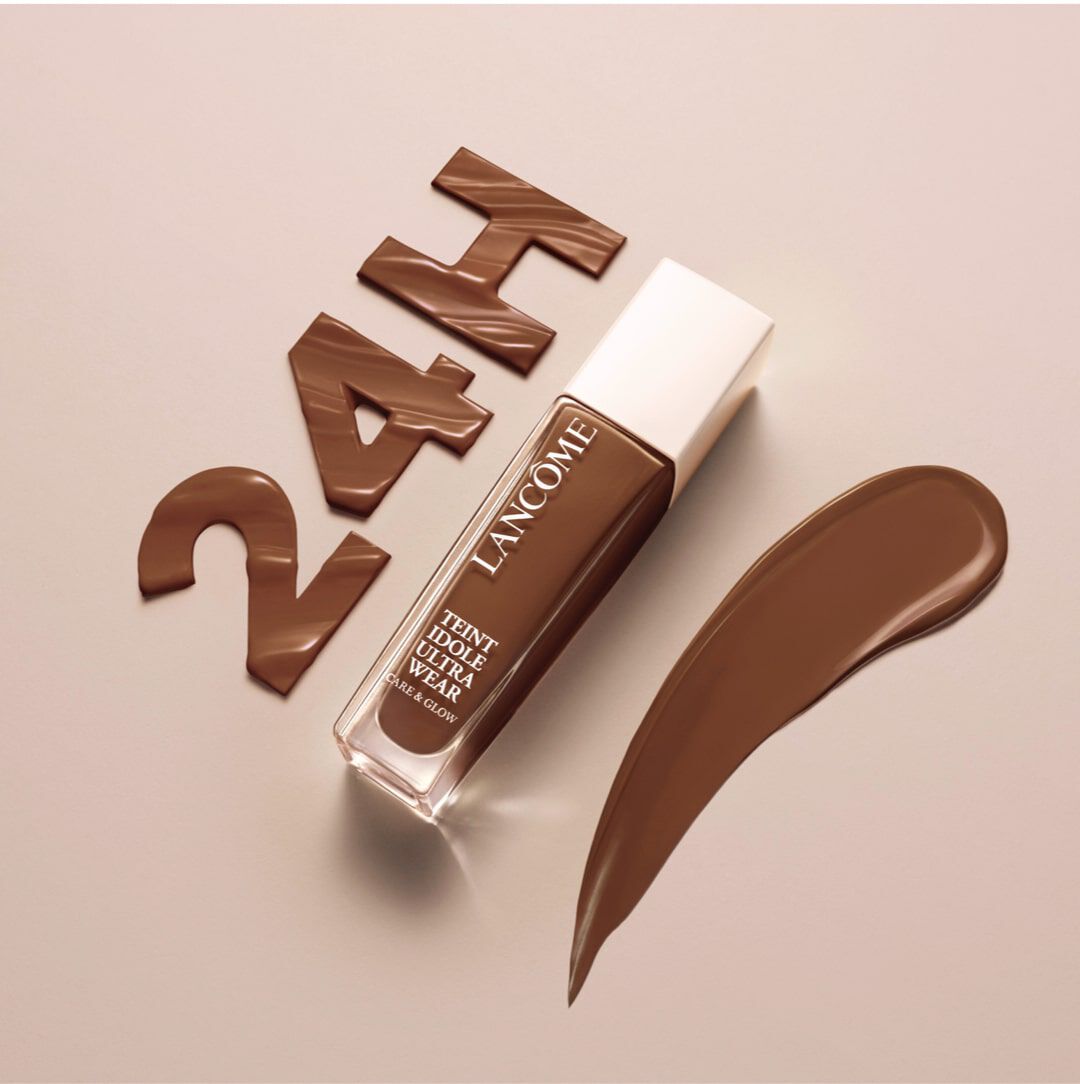 A bottle of Lancome foundation in a dark brown shade is displayed alongside a brown swatch and the text "24H" in stylized letters. The background is a neutral beige color.