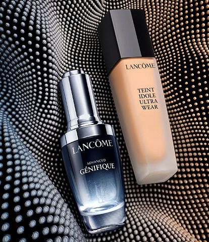 Two Lancome skincare products are displayed against a textured, wavy background. On the left is a bottle of Advanced Genifique serum, and on the right is a foundation labeled Teint Idole Ultra Wear.