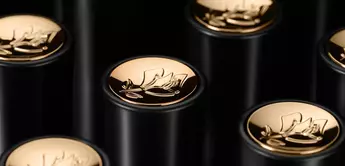 Close-up image of black cylindrical tubes with gold floral logo caps arranged in a visually appealing pattern.