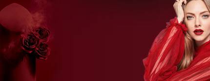 A woman in a dramatic red outfit poses next to a red product with roses, set against a dark red background. Her makeup features bold red lips, and she has long, flowing hair.