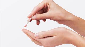 A person is holding a small spatula over one hand, preparing to transfer a small amount of product or cream from the spatula to their palm.