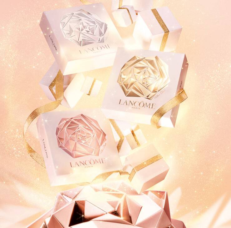 Three elegantly designed gift boxes in white and gold with a geometric rose motif, surrounded by smaller gift boxes and a sparkling background. The boxes are labeled "Lancome Paris."