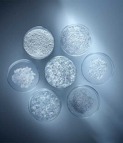 Alt text: A collection of seven glass bowls filled with various types of transparent crystals, arranged in a circular pattern against a dark background with soft lighting.