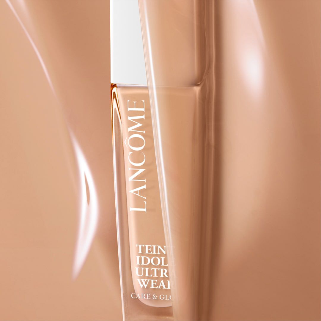 A close-up of a Lancome foundation bottle partially obscured, featuring elegant packaging with a neutral beige background and the text "Teint Idole Ultra Wear."