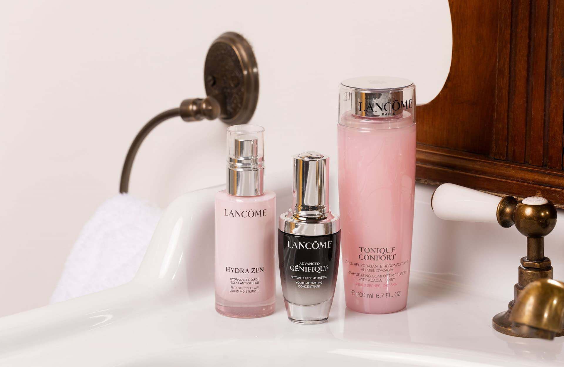 Three bottles of Lancome skincare products, including Hydra Zen, Advanced Genifique, and Tonique Confort, displayed on a bathroom countertop.