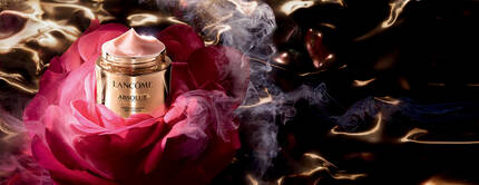 A luxurious jar of Lancome Absolue cream sits atop a large, vibrant rose, surrounded by swirling smoke and a glossy, dark background.