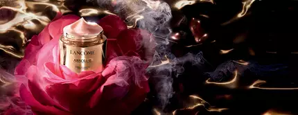 A luxurious jar of Lancome Absolue cream sits atop a large, vibrant rose, surrounded by swirling smoke and a glossy, dark background.