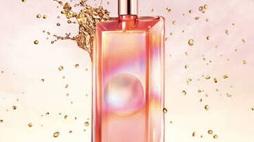 A sleek, rectangular perfume bottle with a metallic cap, featuring a gradient design in shades of pink and orange. Behind the bottle, droplets and splashes of liquid create a dynamic background.