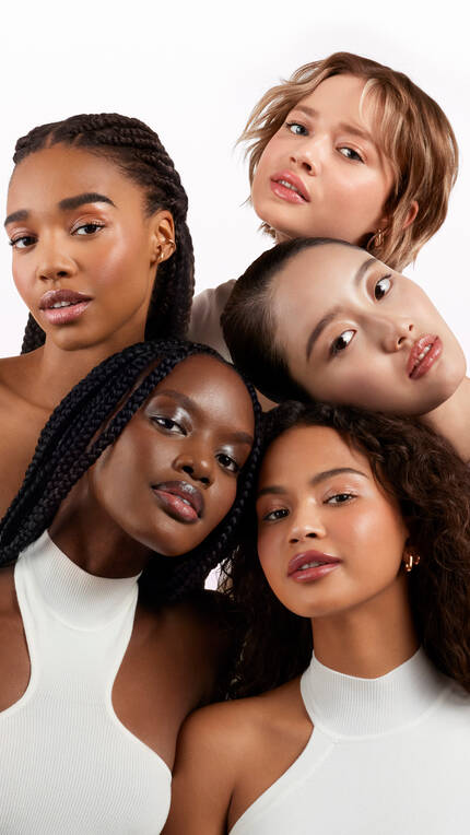 A diverse group of five women with varying hairstyles and facial features, arranged in a close-up composition against a light background. They are looking towards the camera with soft expressions.