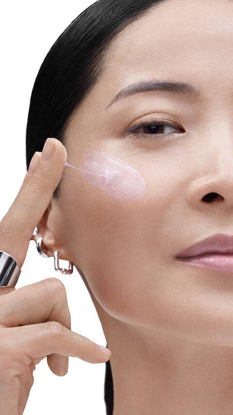 Model applying Lancome product to her cheek, highlighting radiant, plump skin.