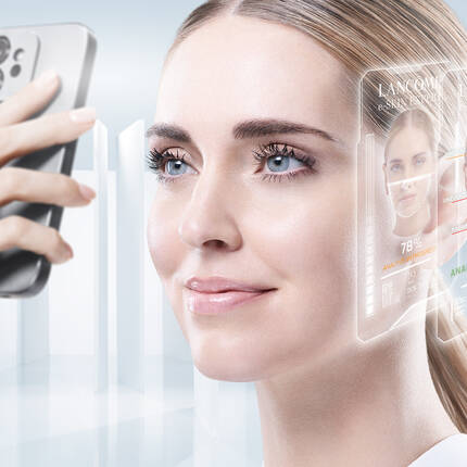 A woman with long hair is having her skin analyzed with a handheld device, while digital screens displaying skincare information and products appear next to her face. The background is a soft blue.