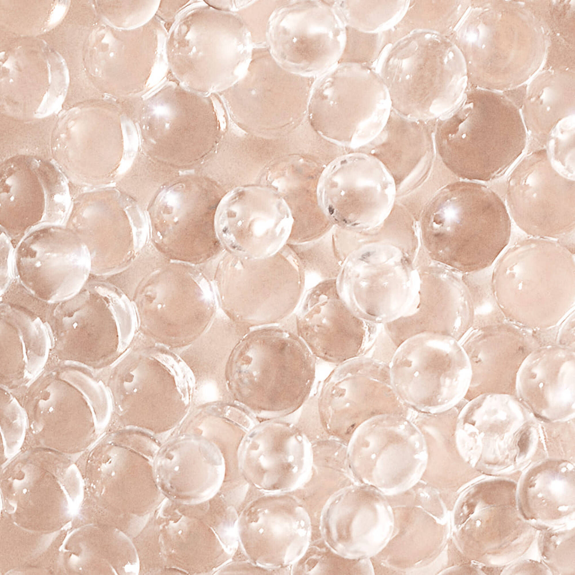 A close-up of small, transparent spheres arranged closely together, resembling beads or water droplets on a light background.