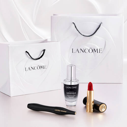 A white gift bag with the Lancome logo, accompanied by a bottle of serum, a tube of red lipstick, and a pair of tweezers on a light background.