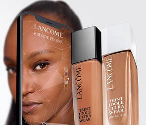 A close-up image featuring a sleek bottle of Lancome's "Teint Idole Ultra Wear" foundation alongside a smartphone displaying the product, with a model's face partially visible in the background.