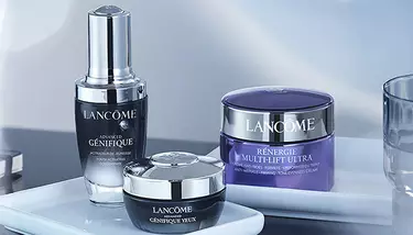 Three Lancome skincare products (Genifique serum, Genifique eye cream, and Renergie Multi-Lift Ultra) are displayed on a white tray.