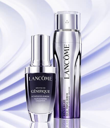 Two skincare products from Lancome are displayed against a soft, wavy blue background. One is a serum, while the other is likely a moisturizer or treatment, both elegantly designed with sleek packaging.