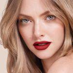 Close-up of a woman with wavy blonde hair and striking red lipstick, showcasing flawless skin and captivating blue eyes.