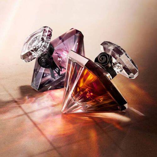 A woman with long brown hair holds a perfume bottle close to her face, eyes closed, exuding elegance and allure.