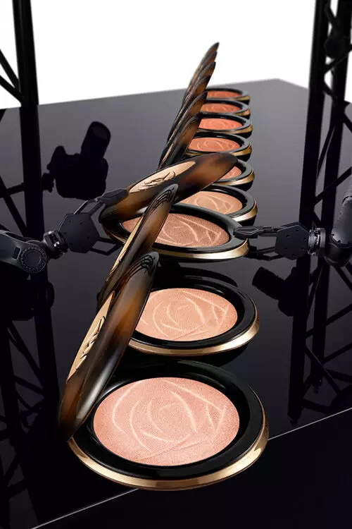 Two compact powders with a rose design on the surface, set against a reflective black background.