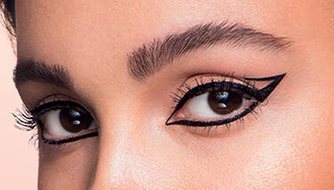 A close-up of a person's eyes with creative black winged eyeliner, featuring a unique open-wing design on one eye.