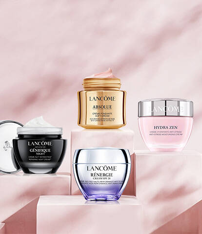 A collection of four Lancome skincare cream jars displayed on pedestals against a soft pink marble background.