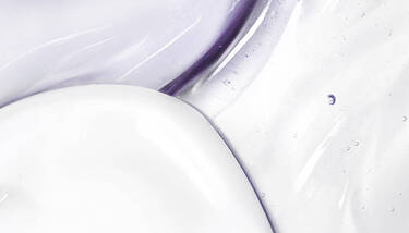 A macro shot of swirled white cream and clear gel with purple undertones and small bubbles.