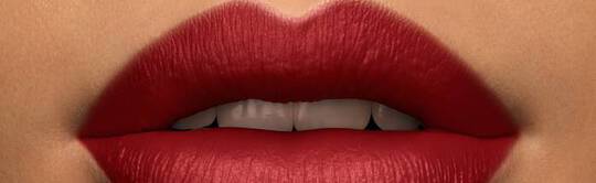 Close-up of a person's lips painted in bold red lipstick, with a neutral skin tone in the background.
