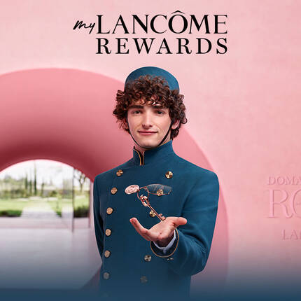 A young person in a stylish blue outfit stands in front of a circular pink backdrop, holding a small flower. The background displays the text "L'Ombre Edition ROSE Lancome."