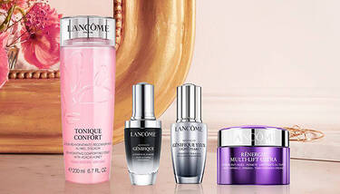 A collection of four Lancome skincare products—Tonique Confort, Advanced Genifique, Genifique Yeux Light-Pearl, and Renergie Multi-Lift Ultra—are displayed on a light background with floral elements.