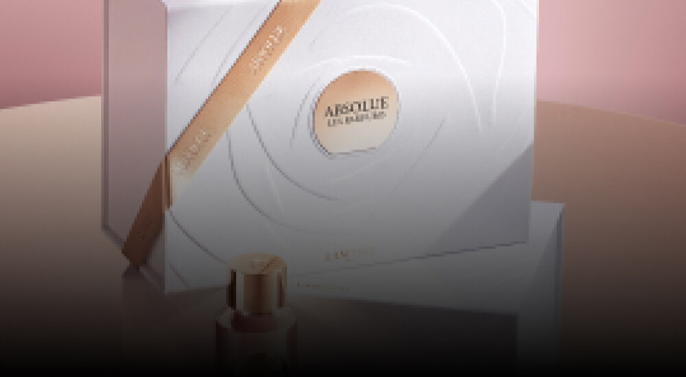 A stylish image showcasing two elegant bottles of Lancome's Absolue perfume, placed on top of a white, decorative box with subtle gold accents. The background features soft pink tones, enhancing the luxurious presentation.