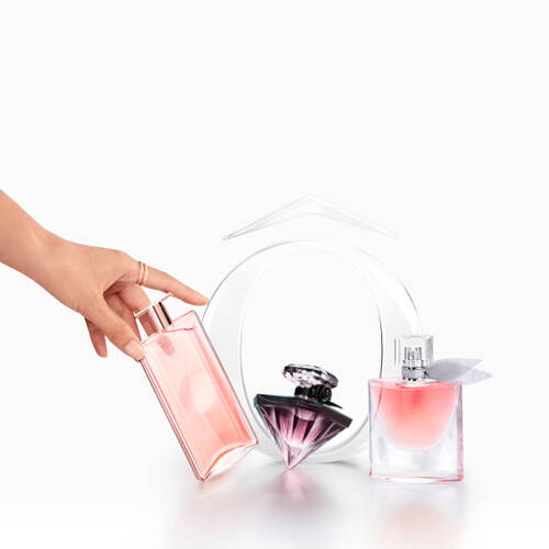 A hand holds a transparent perfume bottle, while two other stylish perfume bottles are displayed on a sleek surface. The background is a gradient from light to dark.