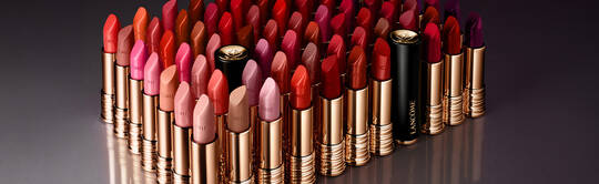 A collection of various shades of lipsticks arranged in rows, featuring vibrant reds, pinks, and purples, with gold and black packaging.