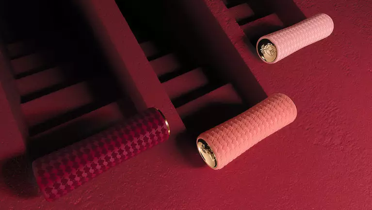 Three textured bike grips in pink and burgundy are mounted on a dark red wall, showcasing a modern design aesthetic.