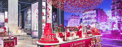 A vibrant retail store filled with pink and red rose-themed decorations, featuring beautifully arranged displays of products. The walls are adorned with colorful visuals, creating a festive atmosphere.