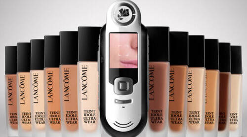 A collection of Lancome Teint Idole Ultra Wear foundation bottles lined up with a digital shade-matching device in the center.