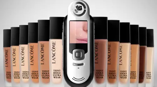A collection of Lancome Teint Idole Ultra Wear foundation bottles lined up with a digital shade-matching device in the center.