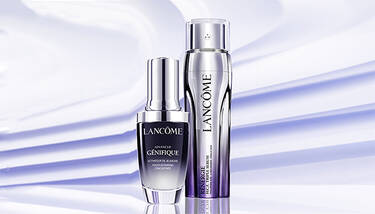 Two Lancome serums, Advanced Genifique and Renergie H.C.F. Triple Serum, are showcased against a light purple background with diagonal shadow stripes.
