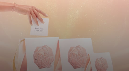 A hand drops a card reading 'From Sadie with love' into a stylish gift bag, set against a soft, sparkly background.